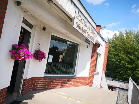 Wejście do Bistro na Żwirki z szyldem „Obiady domowe” i kwiatami